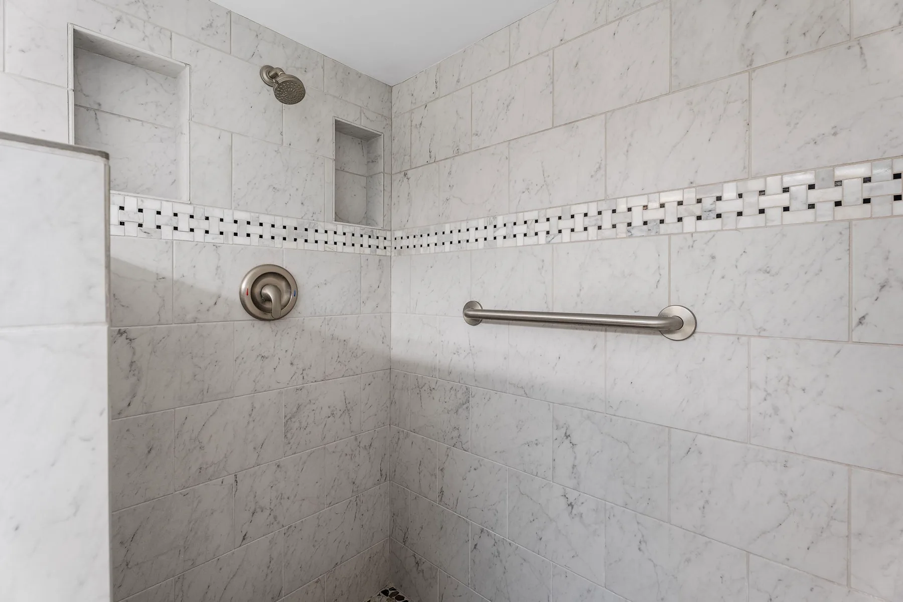 Una zona de ducha con azulejos y una barra de apoyo en la pared.
