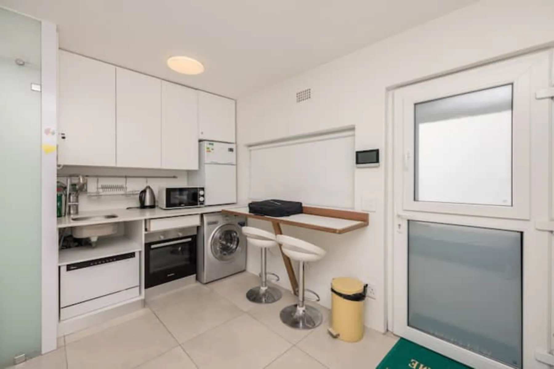 Una cocina compacta con una barra y dos taburetes junto a una puerta acristalada.