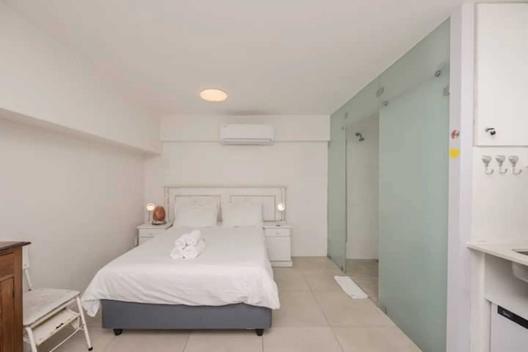 Un dormitorio luminoso con una cama bien arreglada y divisiones de ducha de vidrio.