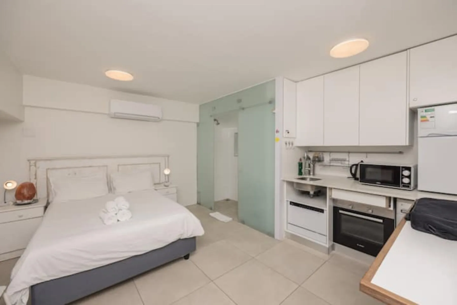 Un dormitorio con una pequeña cocina, una cama y armarios blancos.