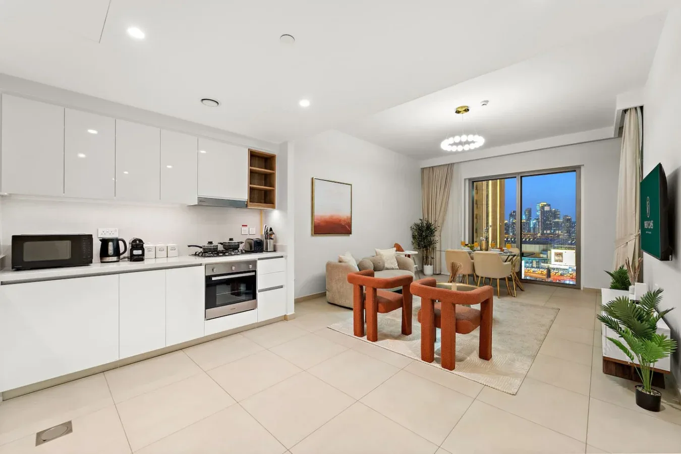 A bright open-plan living and dining area with a white kitchen and city views.
