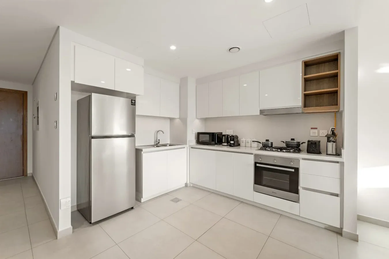 A bright modern kitchen with white cabinets, stainless steel appliances, and a tiled floor.