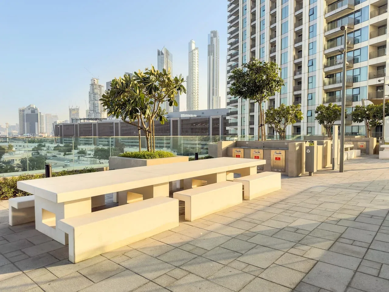 A paved outdoor terrace has long built-in seating, planters, and nearby high-rise buildings.