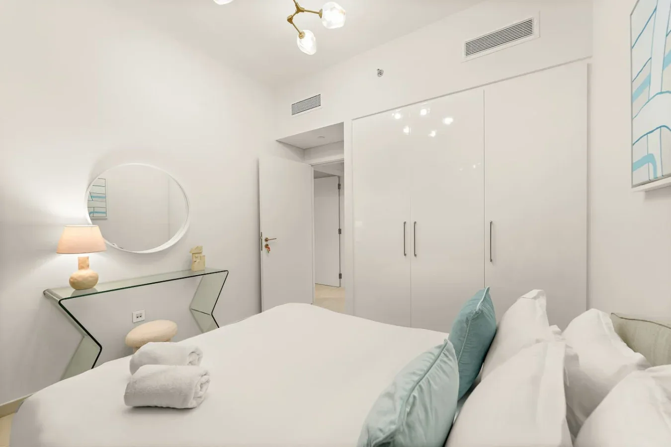 A bright bedroom with a bed, white bedding, and built-in wardrobes.