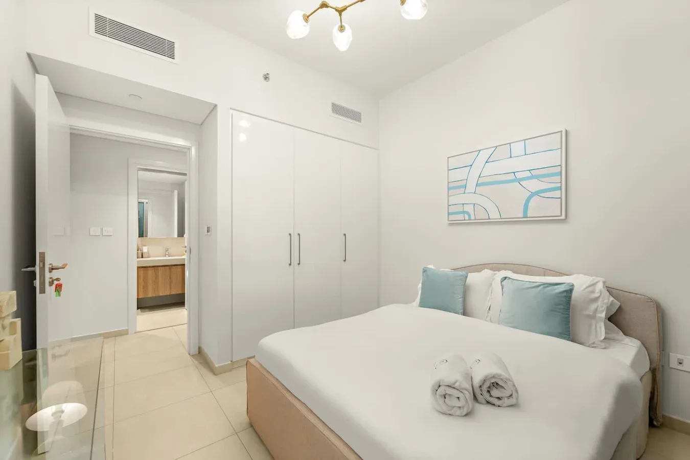 A bright bedroom with a neatly made bed and abstract wall art.