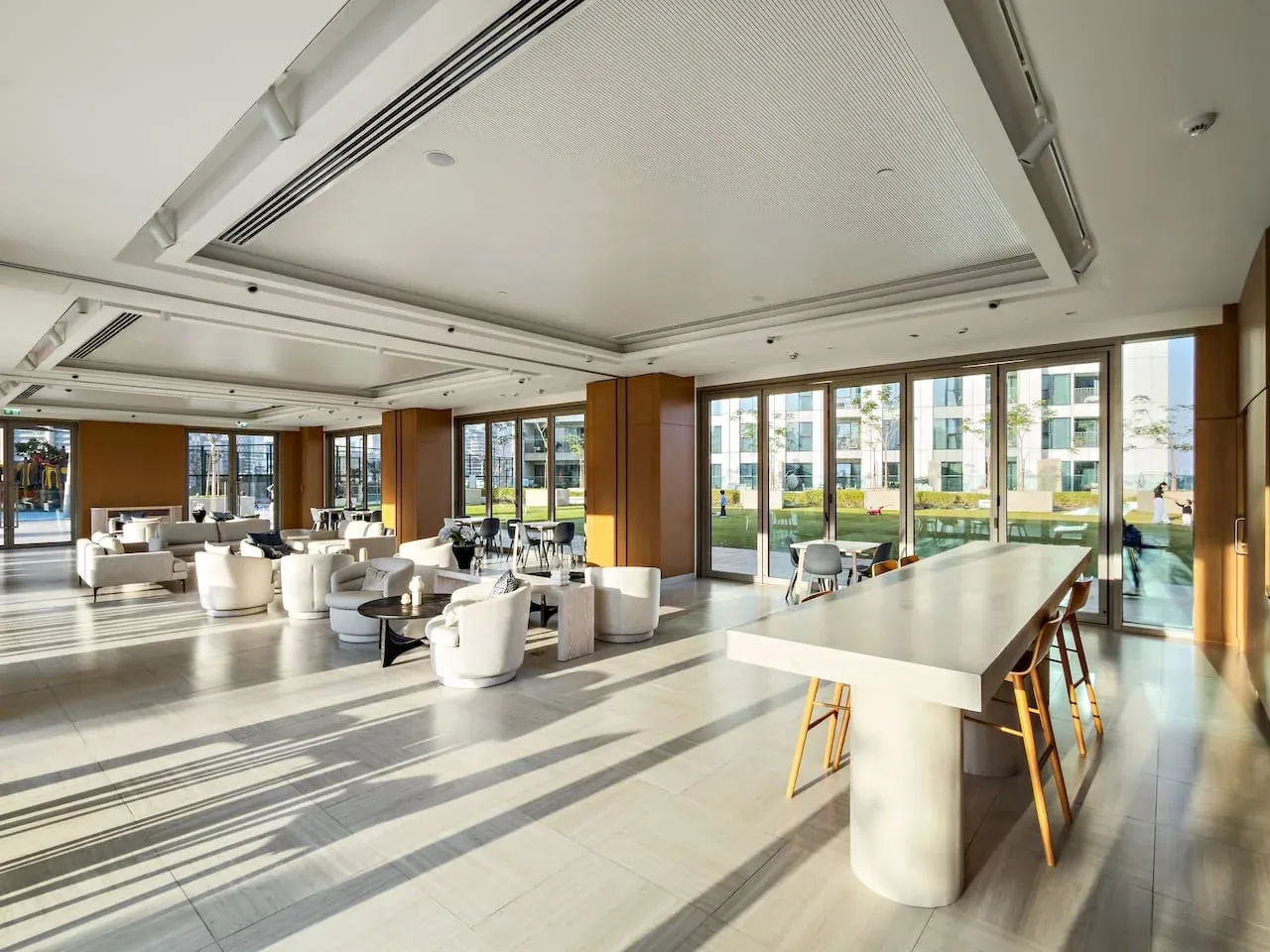 A bright lounge with seating and a long table beside floor-to-ceiling windows.