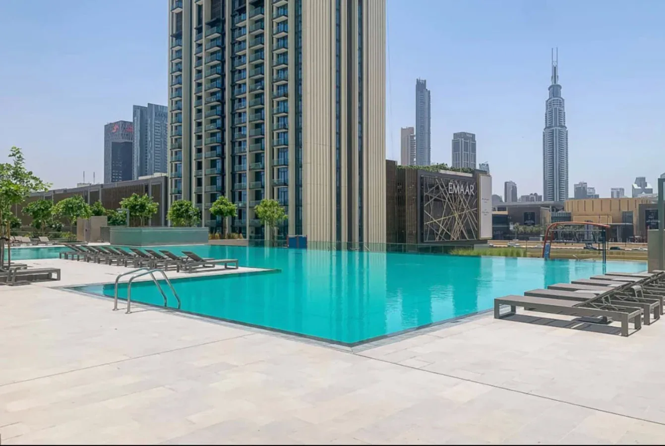 A rooftop swimming pool with lounge seating and city towers in the background.