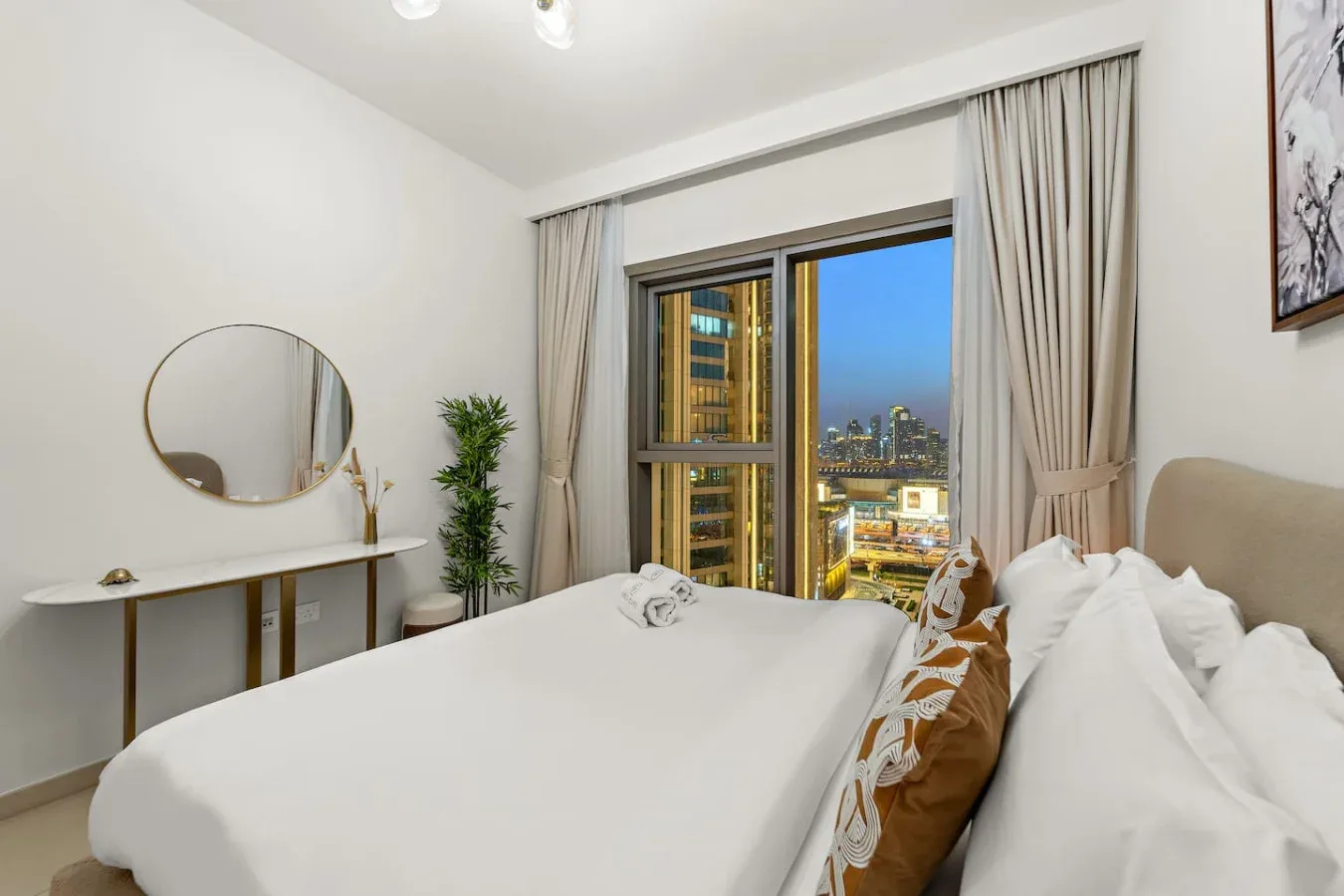 A bright bedroom with a large bed beside a window overlooking city buildings.