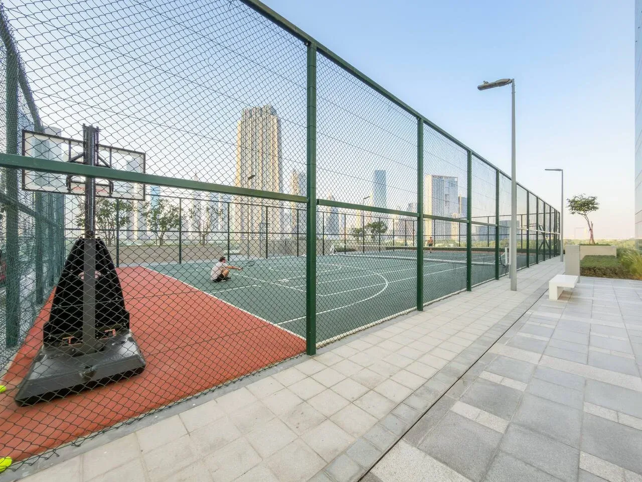 An outdoor sports court with green playing surfaces and surrounding fencing.