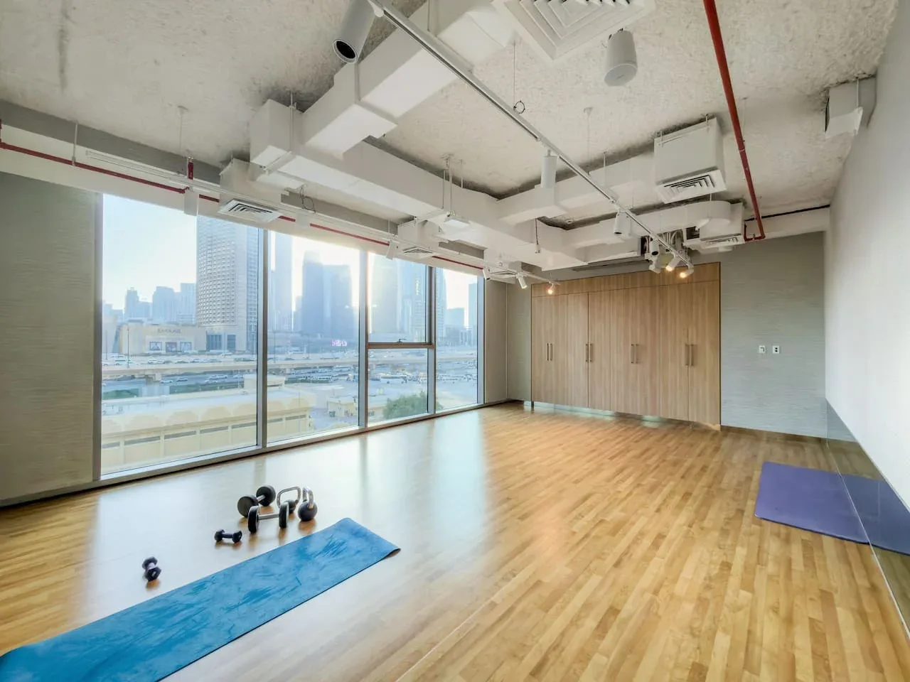A spacious exercise studio has wooden flooring, large windows, and a few workout items.