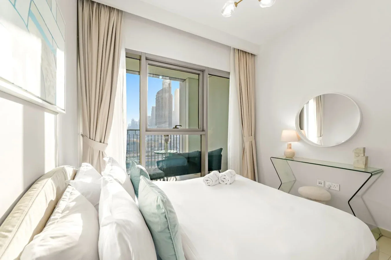 A bright bedroom with a white bed beside a large window.