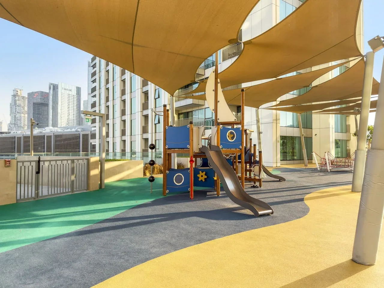 An outdoor playground with slides and climbing equipment beneath shade canopies.