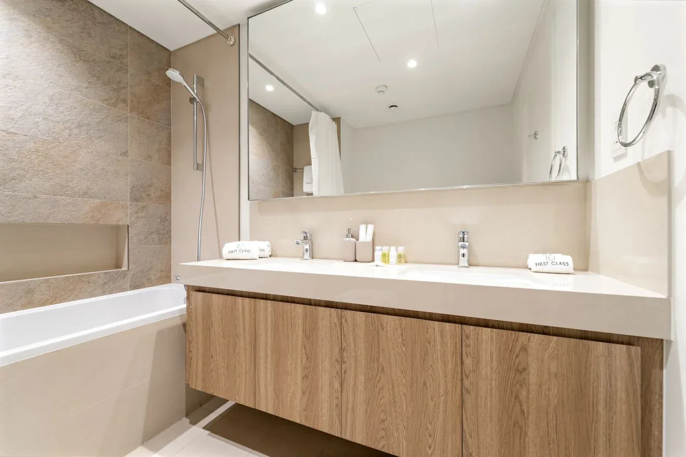A bathroom with a bathtub, shower, and wide vanity beneath a large mirror.