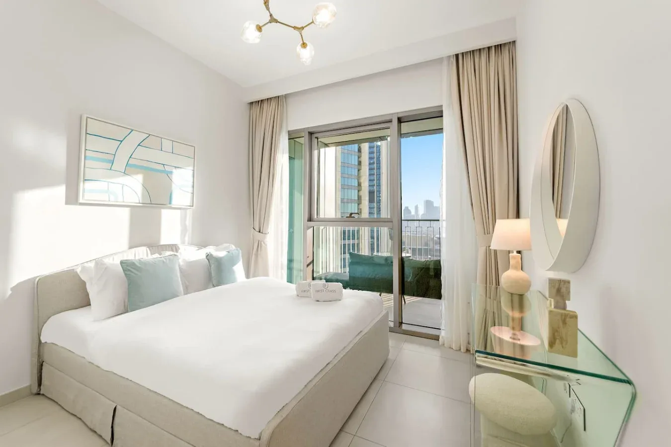 A bright bedroom with a neatly made bed beside glass doors opening onto a balcony.