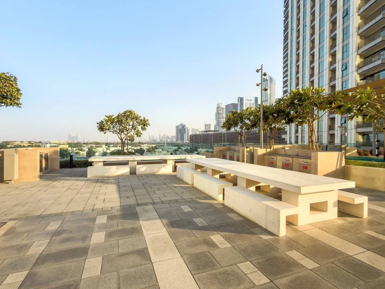 A paved outdoor terrace with long built-in seating beside a high-rise building.
