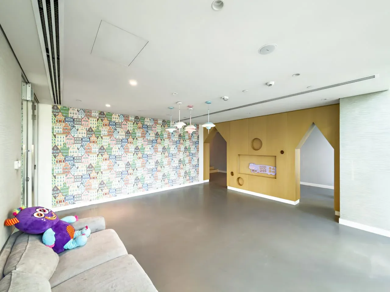 A bright indoor play area has colorful house-patterned wallpaper and seating.