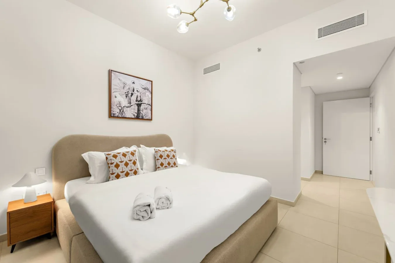 A bright bedroom with a bed, patterned pillows, and a framed wall picture.