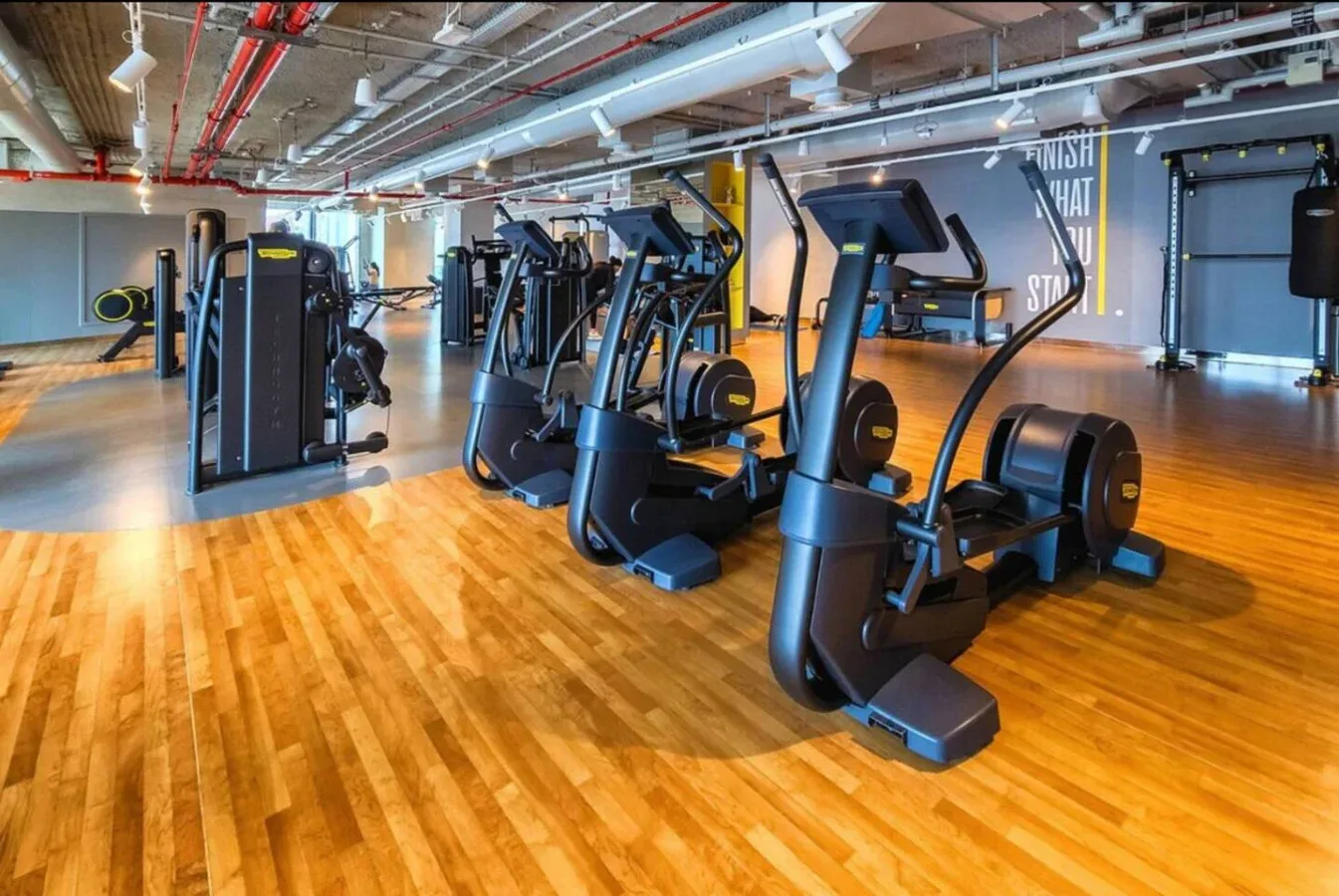 A gym with rows of cardio exercise machines on a wooden floor.