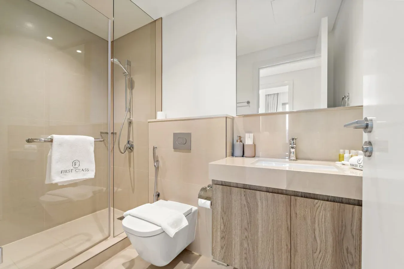 A bright bathroom with a glass shower, toilet, and vanity beneath a large mirror.