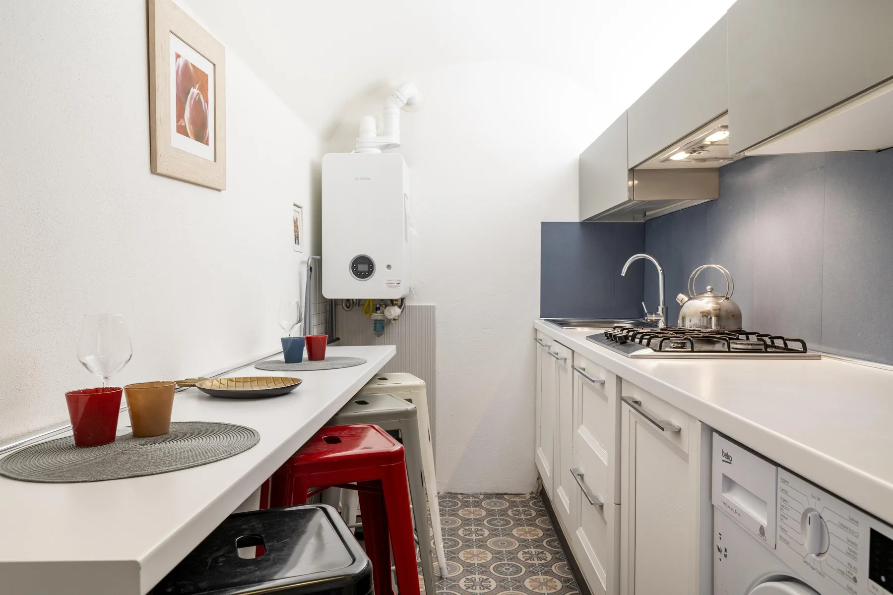 Una cocina estrecha con gabinetes blancos, una estufa de gas y una pequeña barra para comer.