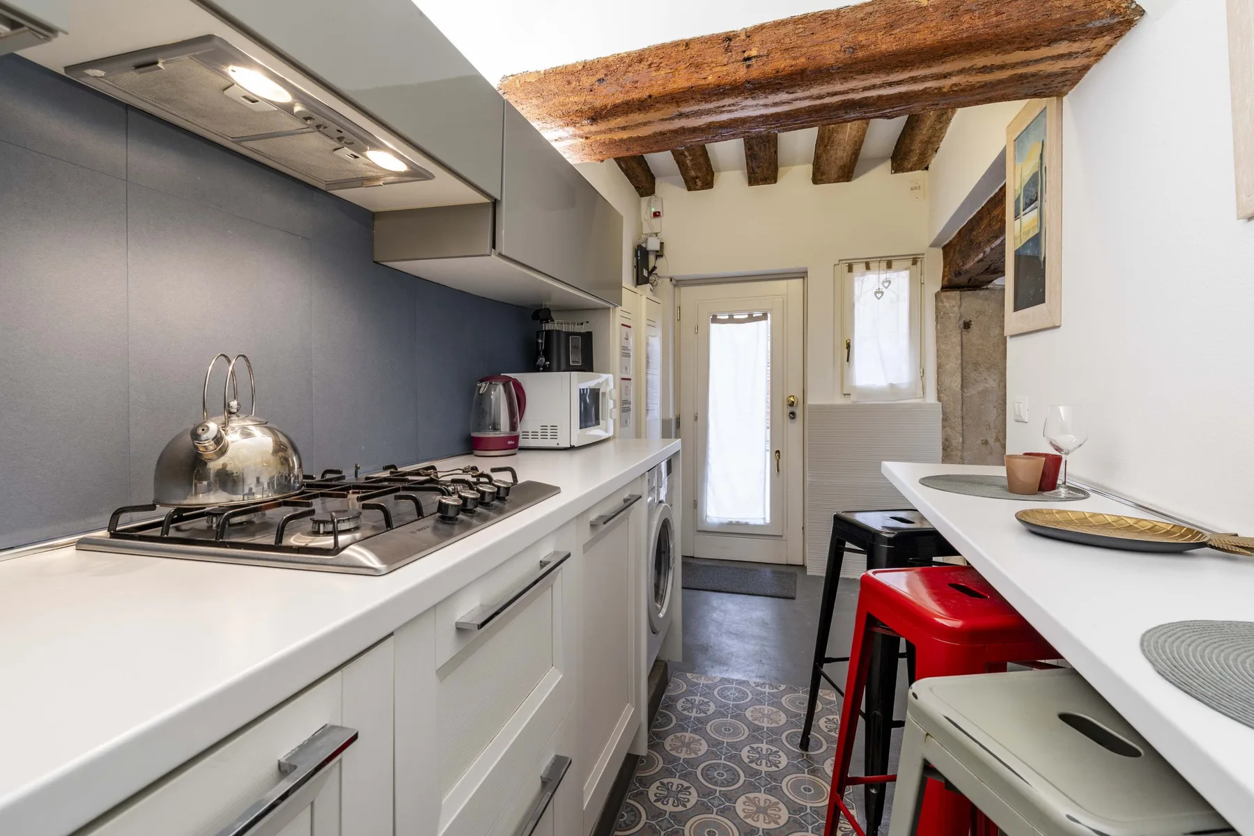 Una cocina estrecha con encimeras blancas, una estufa y vigas expuestas en el techo.