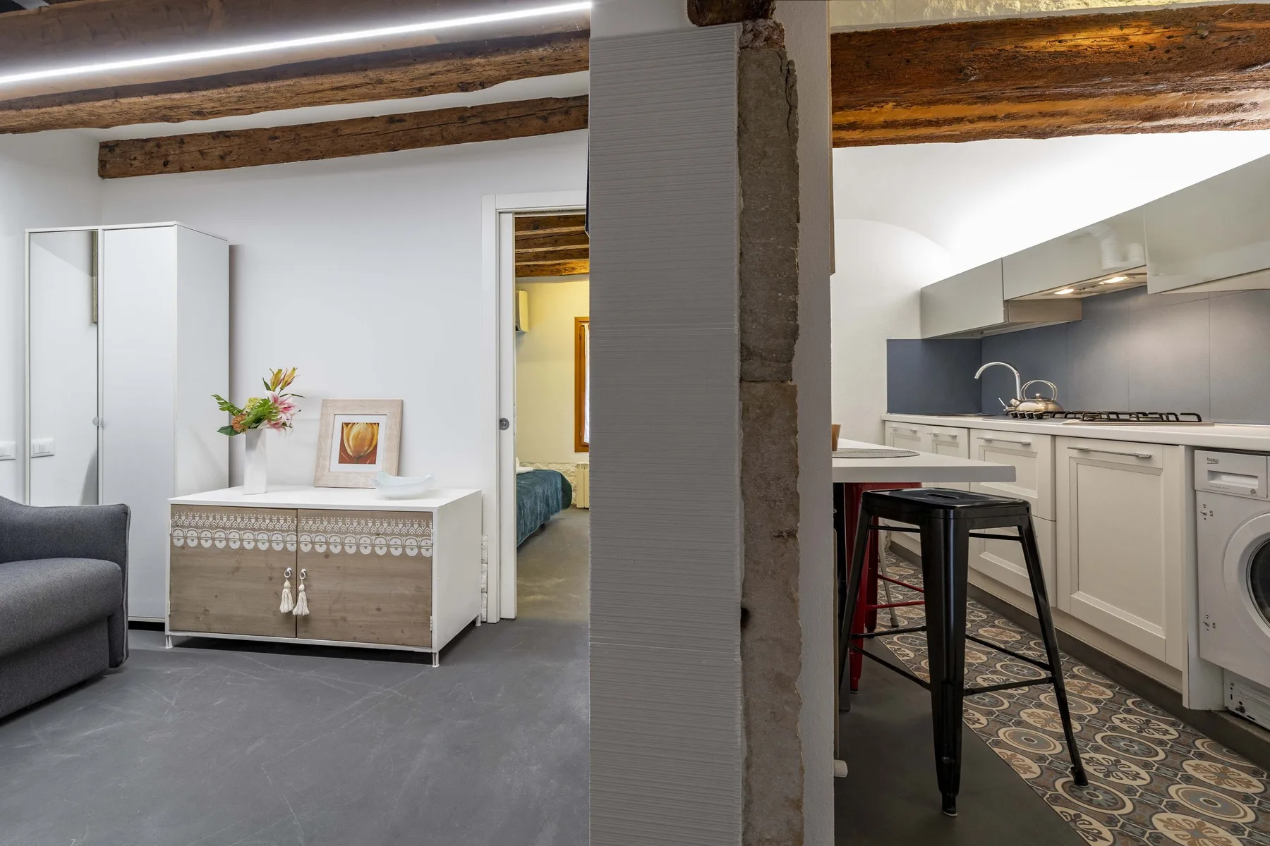Una sala luminosa da a una cocina con una barra y taburetes.