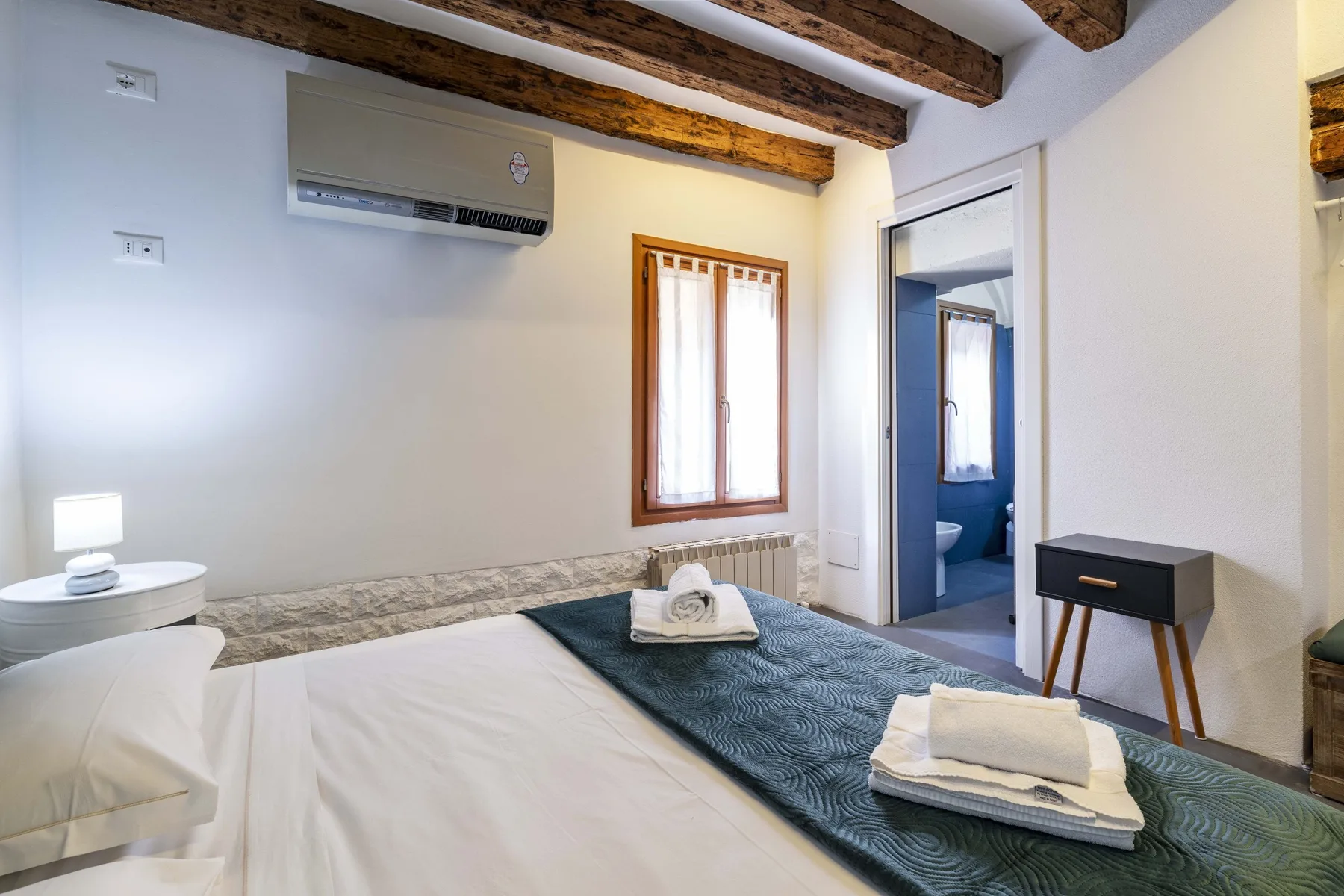 Un dormitorio con una cama, una ventana y una puerta que da a un baño.