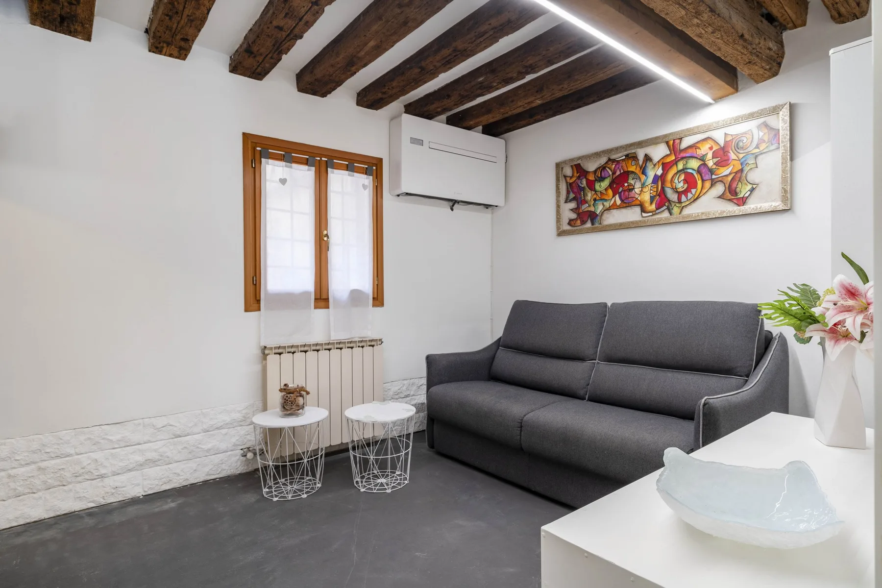 Una sala de estar con un sofá oscuro, mesas pequeñas y vigas expuestas en el techo.