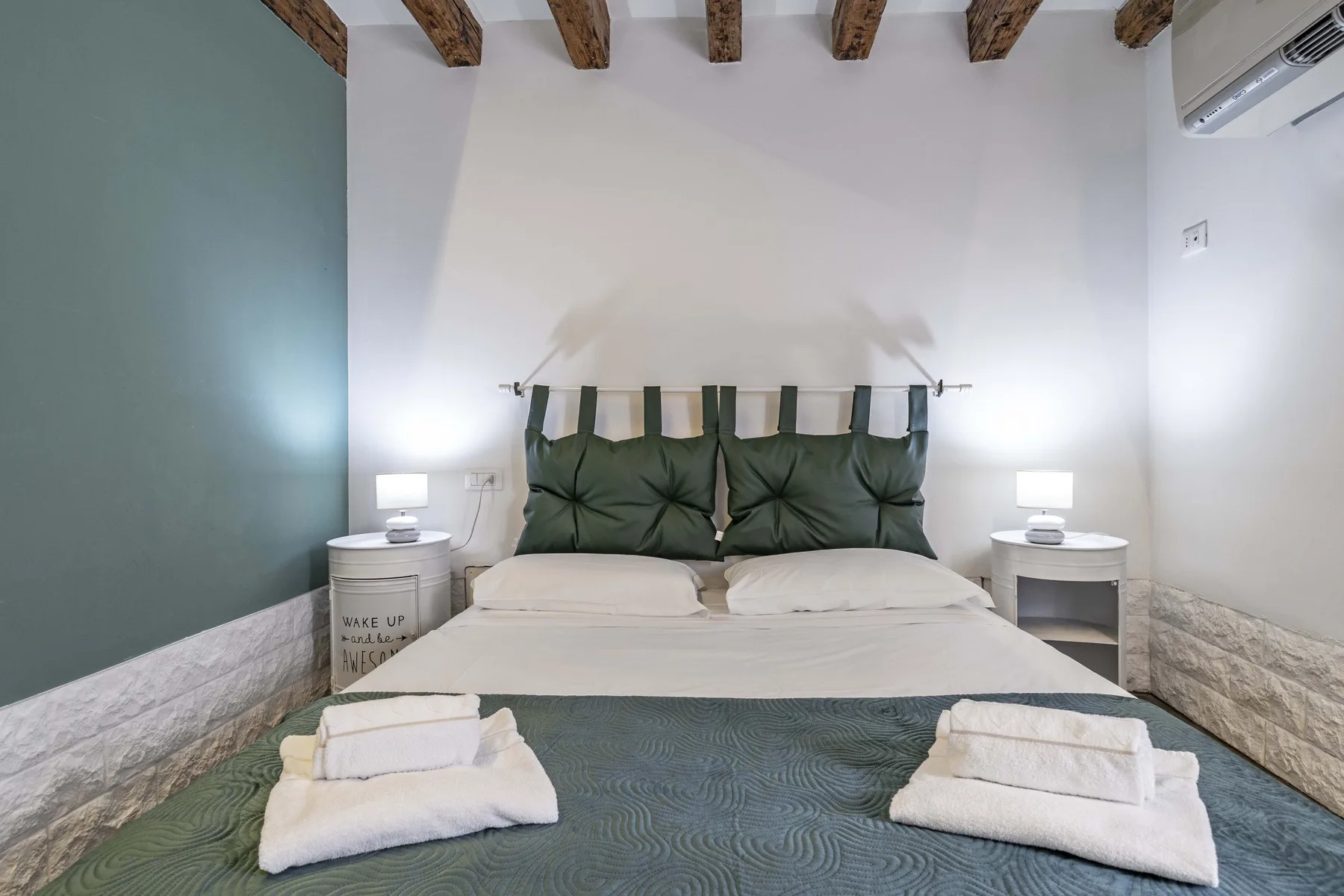 Dormitorio con una cama, cabecero verde oscuro y vigas de techo expuestas.
