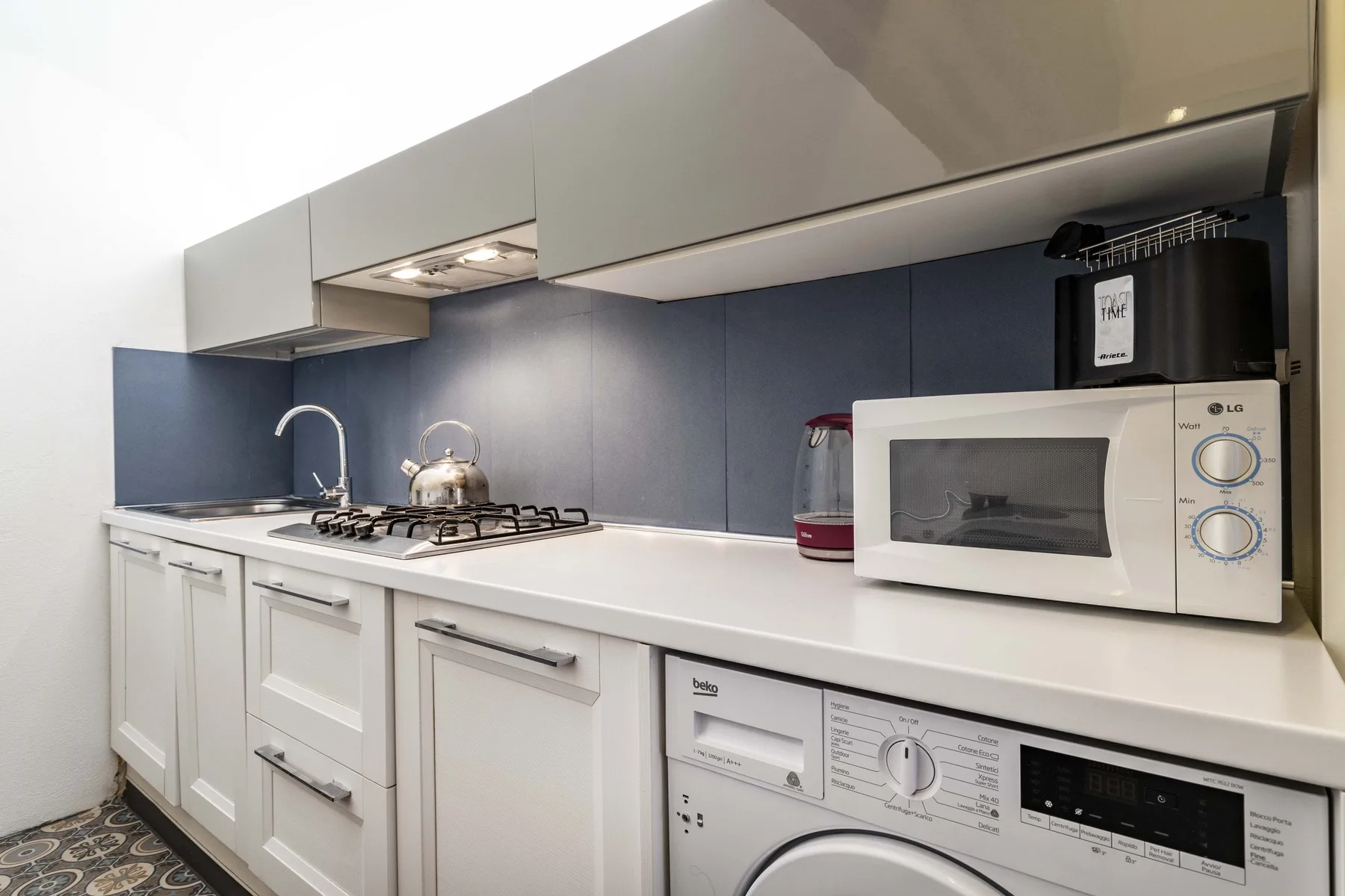 Una cocina compacta con un microondas sobre la encimera y una lavadora debajo.