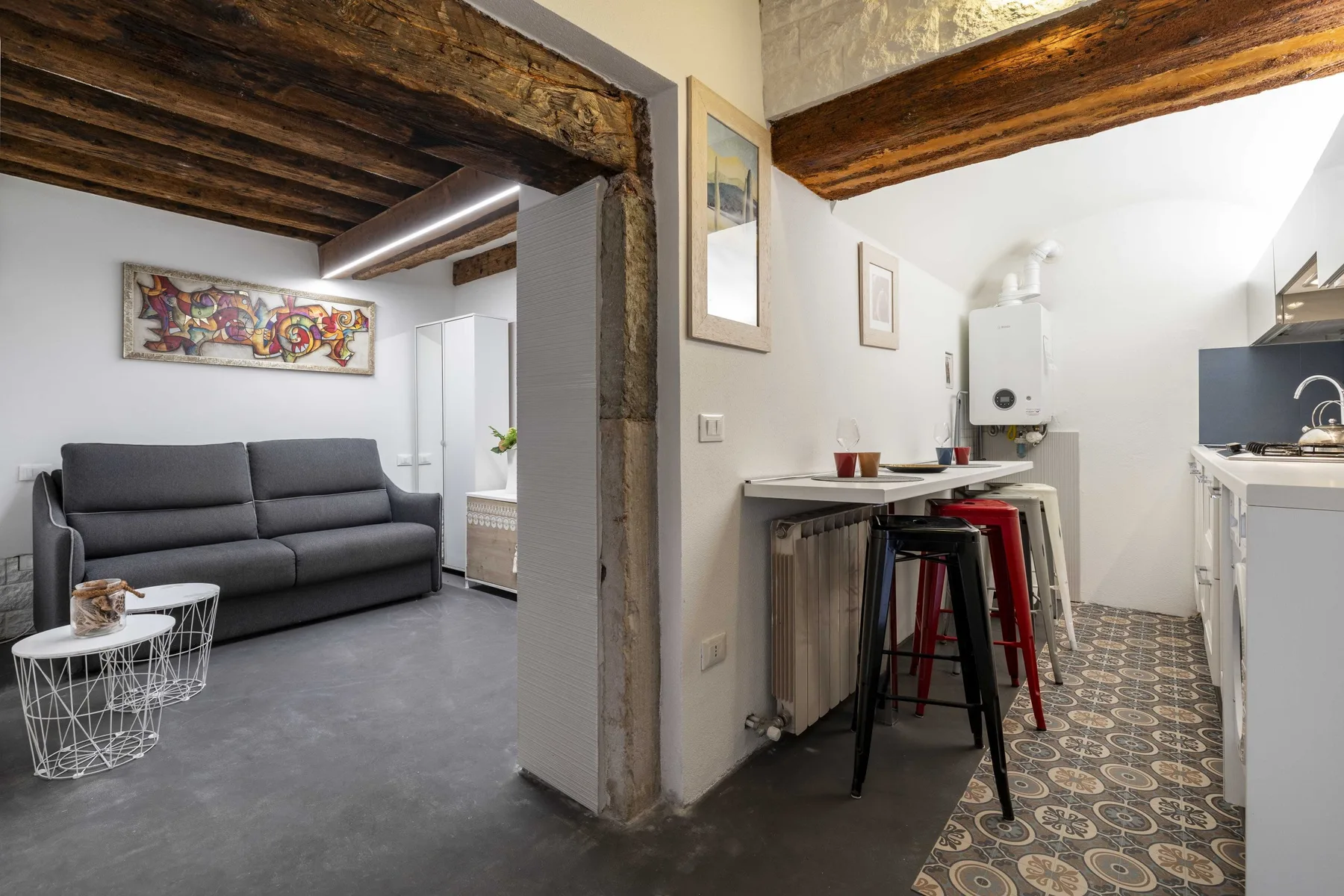 Una zona de estar compacta y una cocina comparten un espacio abierto con vigas de madera vistas.