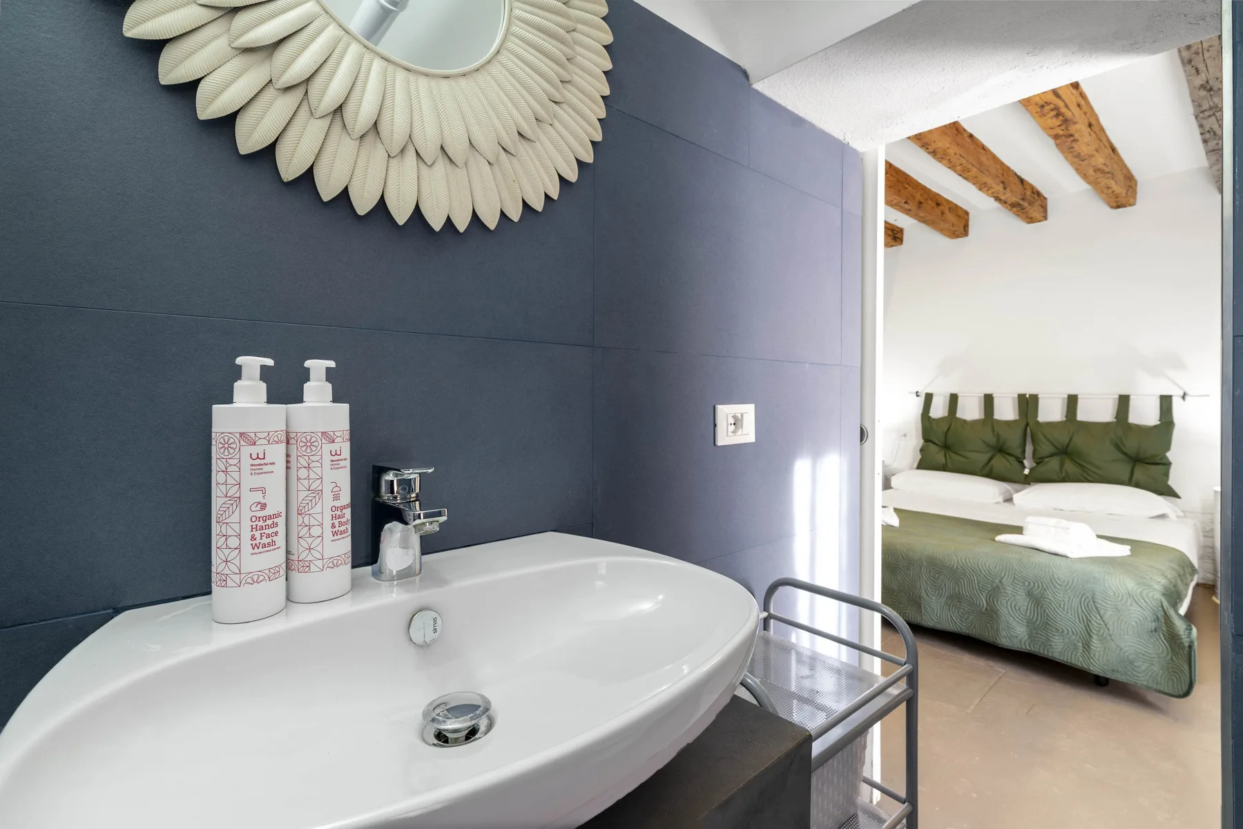 Un lavabo de baño en primer plano da a un dormitorio con una cama.