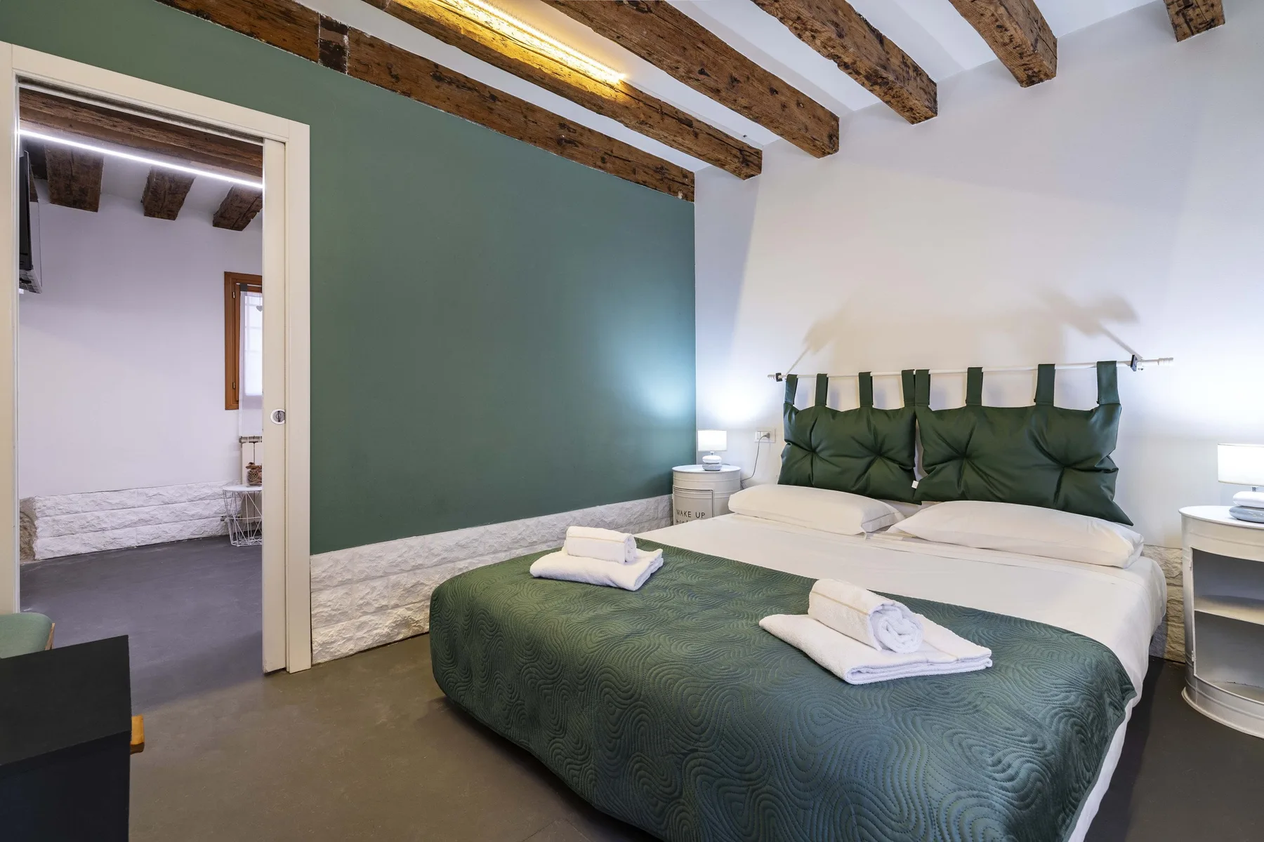 Un dormitorio con colcha verde y un cabecero acolchado verde oscuro.