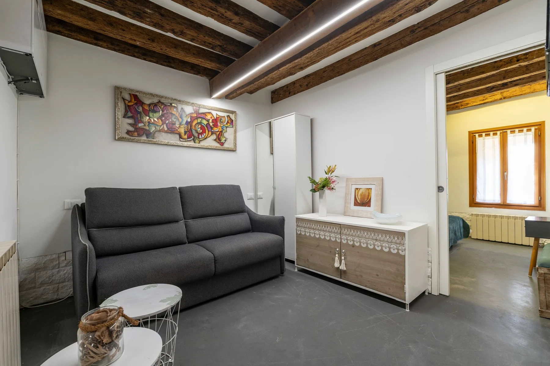 Una sala de estar con asientos oscuros, una mesa baja y vigas de madera a la vista.