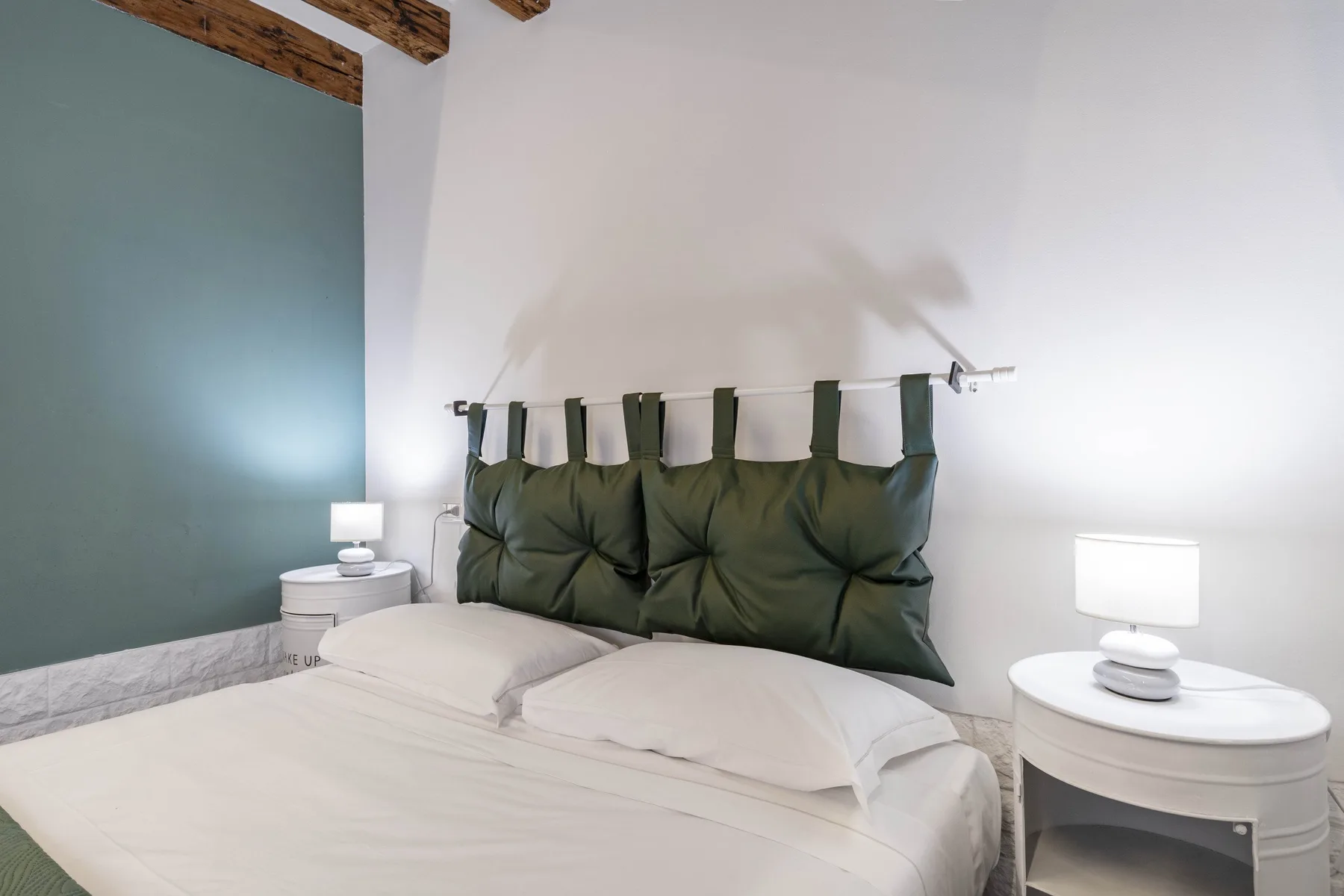 Dormitorio con cama, cabecero verde oscuro y mesitas de noche a juego.
