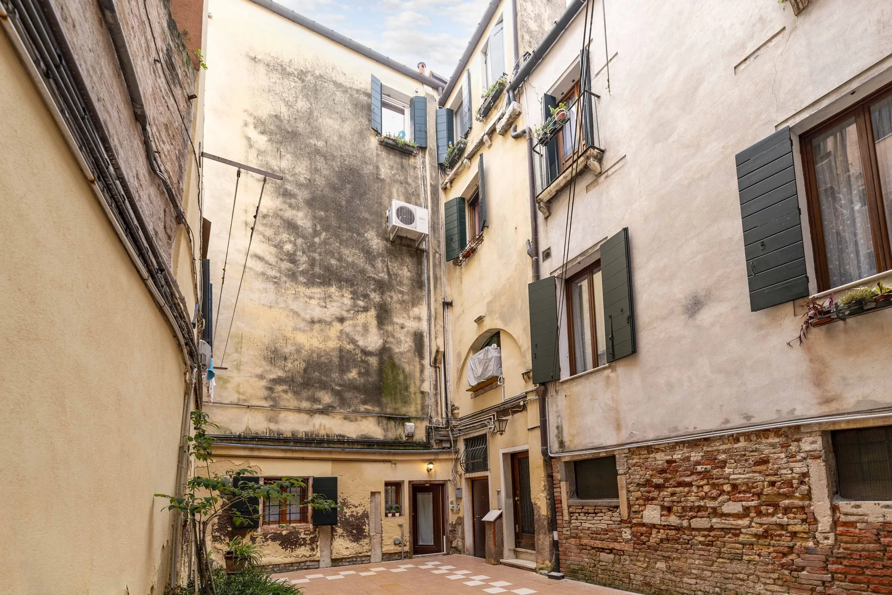 Un pequeño patio rodeado de edificios, con ventanas y persianas verdes.