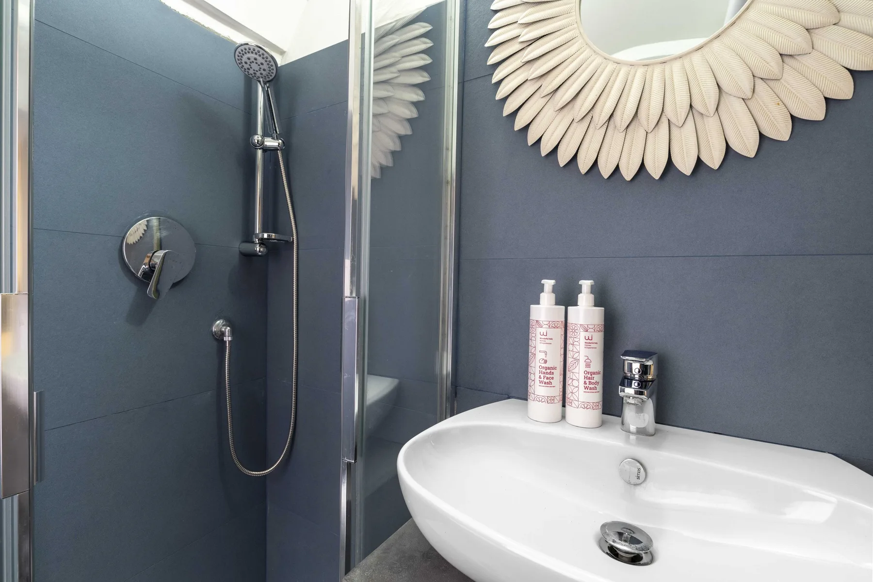Se ven un lavabo y una ducha junto a paredes de azulejos oscuros.