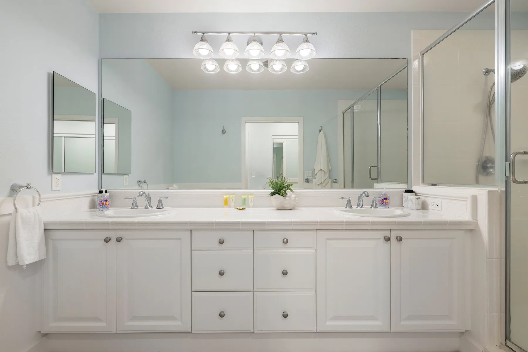 Un baño luminoso cuenta con un largo tocador blanco con lavabos y un espejo grande.