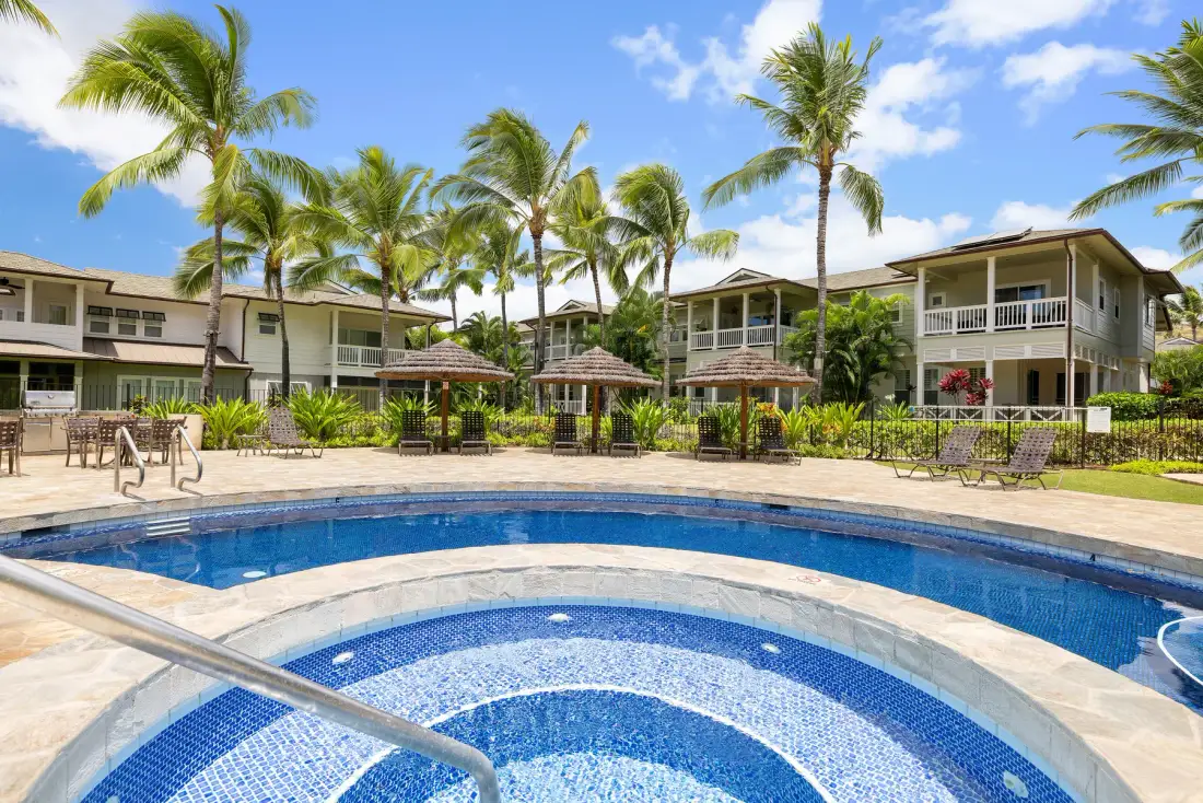 Una piscina curva atraviesa un patio tropical rodeado de palmeras.