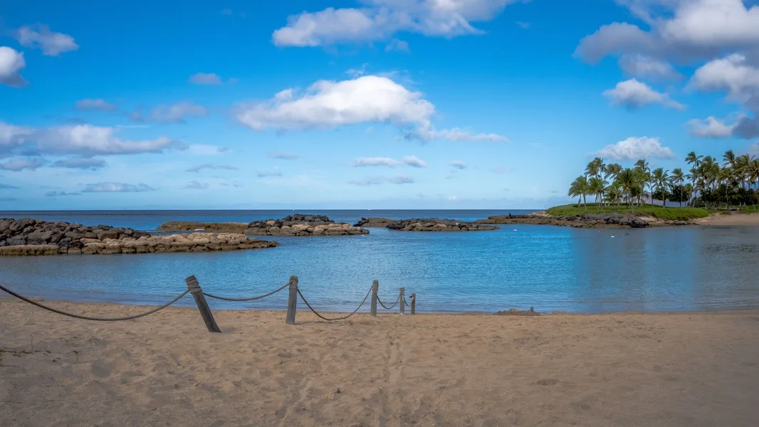 Una playa de arena bordea aguas azules tranquilas bajo un cielo parcialmente nublado.