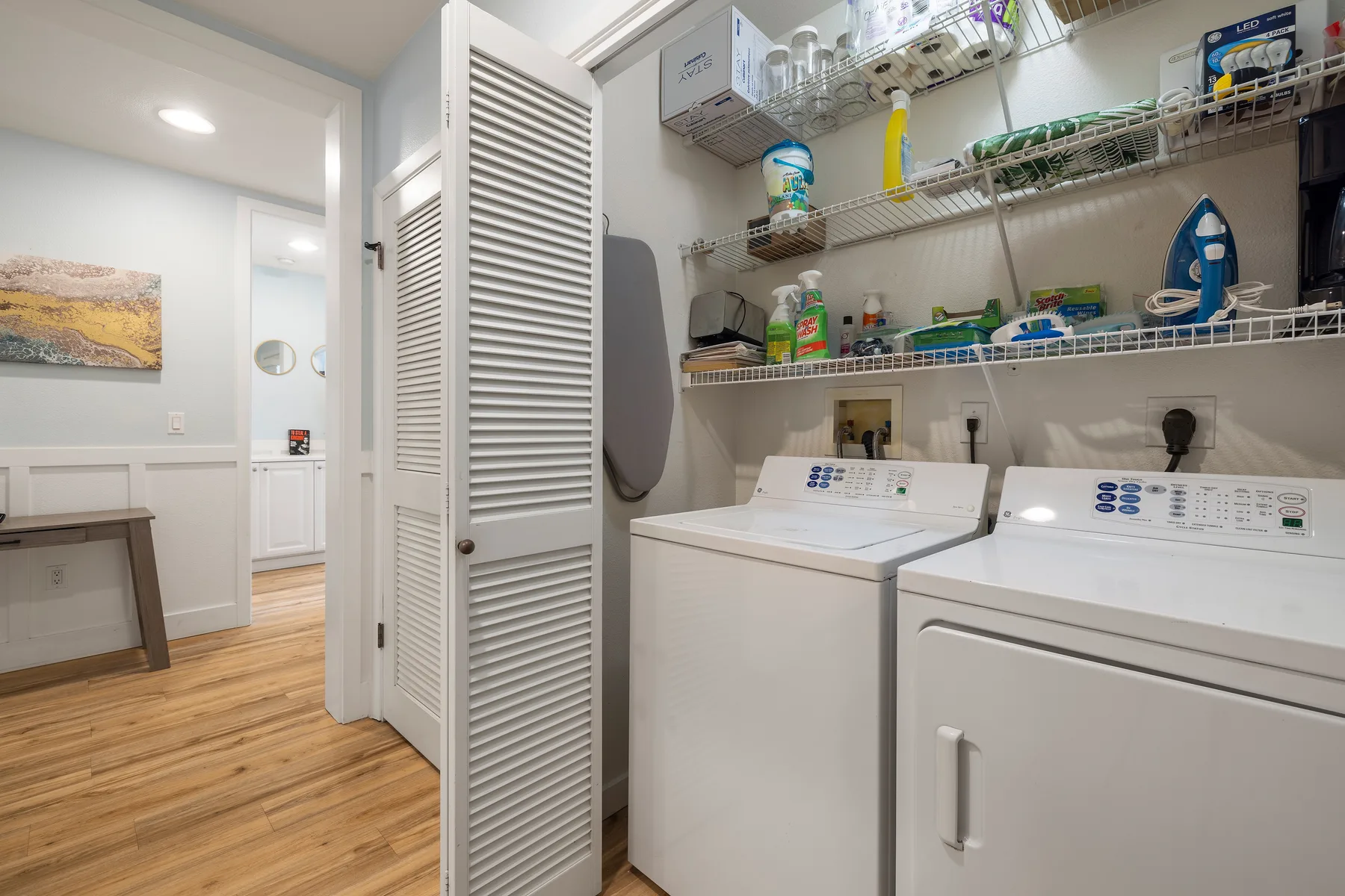 Un cuarto de lavandería con lavadora y secadora bajo estantes de pared.