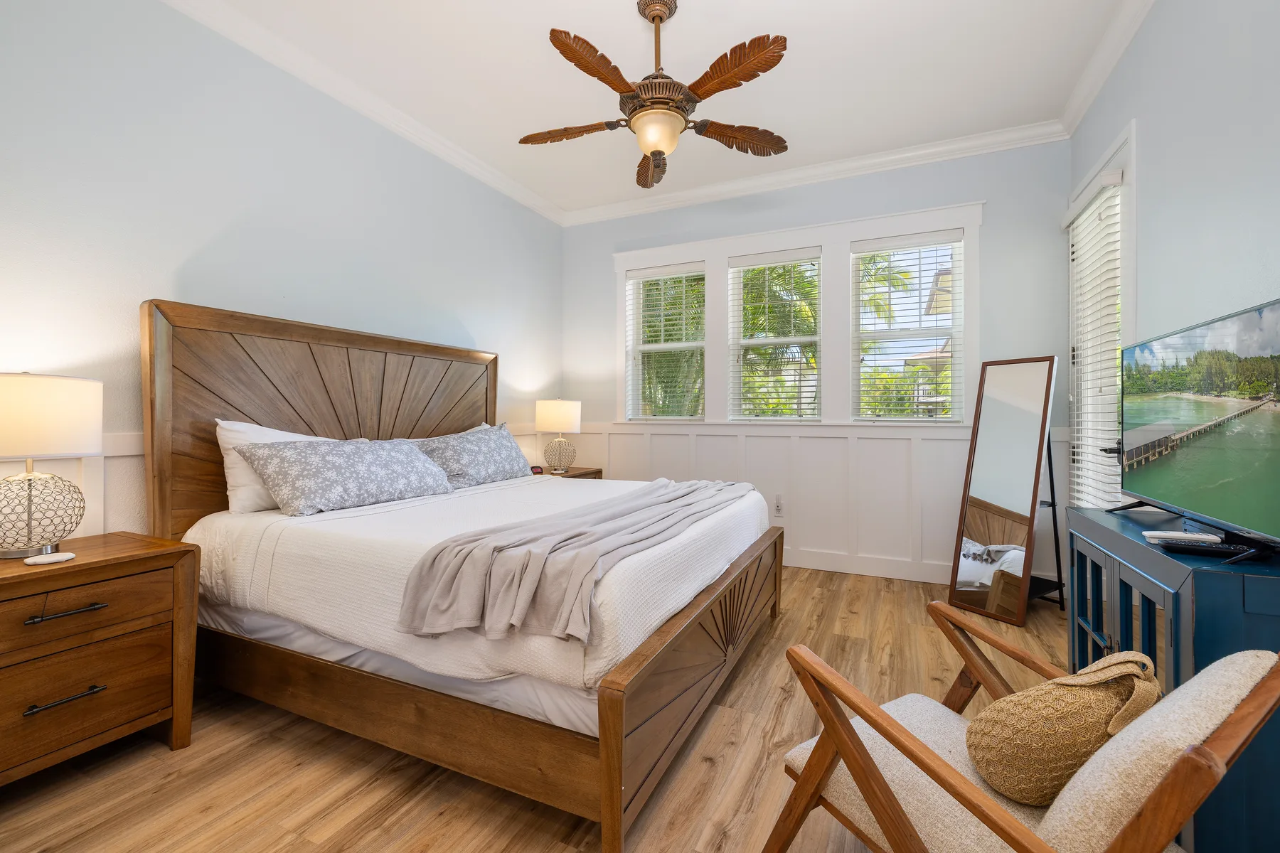 Un dormitorio con una cama de madera, ropa de cama blanca y ventanas en la pared del fondo.