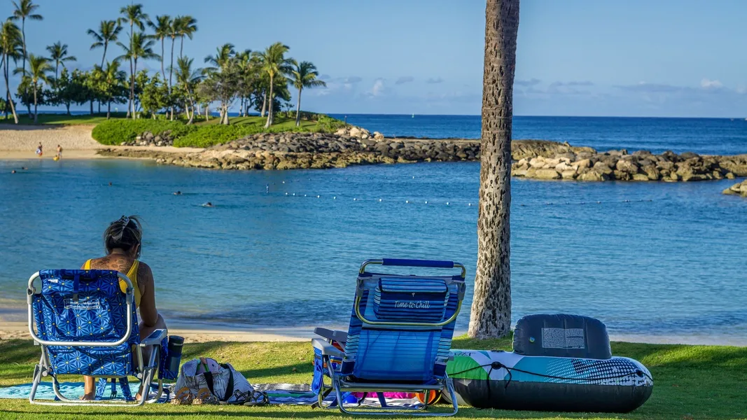 Escena de playa junto al mar, con sillas plegables y una tabla de remo junto al agua.