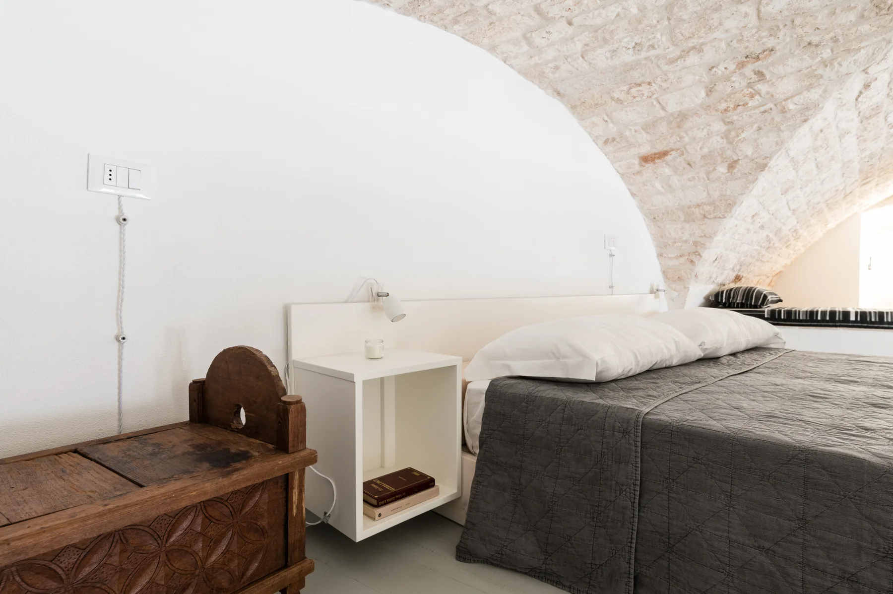 A bedroom with a double bed, bedside table, and wooden chest beneath a curved ceiling.