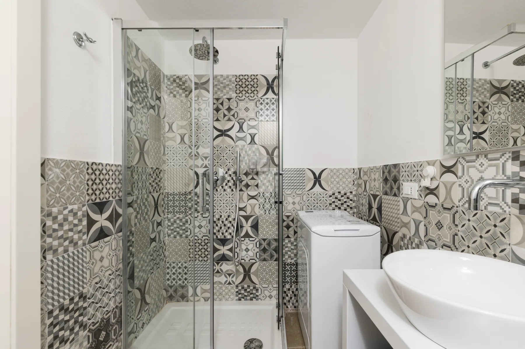 Un baño con azulejos estampados, una ducha de vidrio y un lavabo blanco.