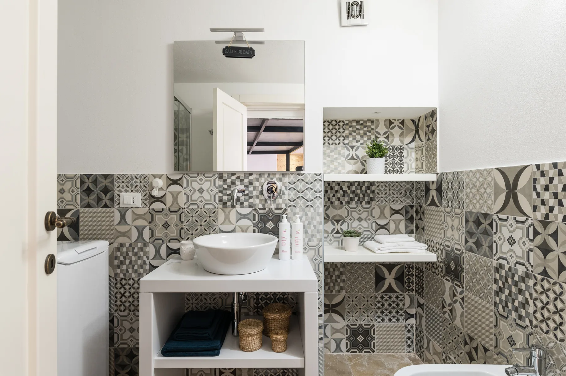Un lavabo de baño con un lavamanos sobrepuesto y paredes de azulejos estampados.