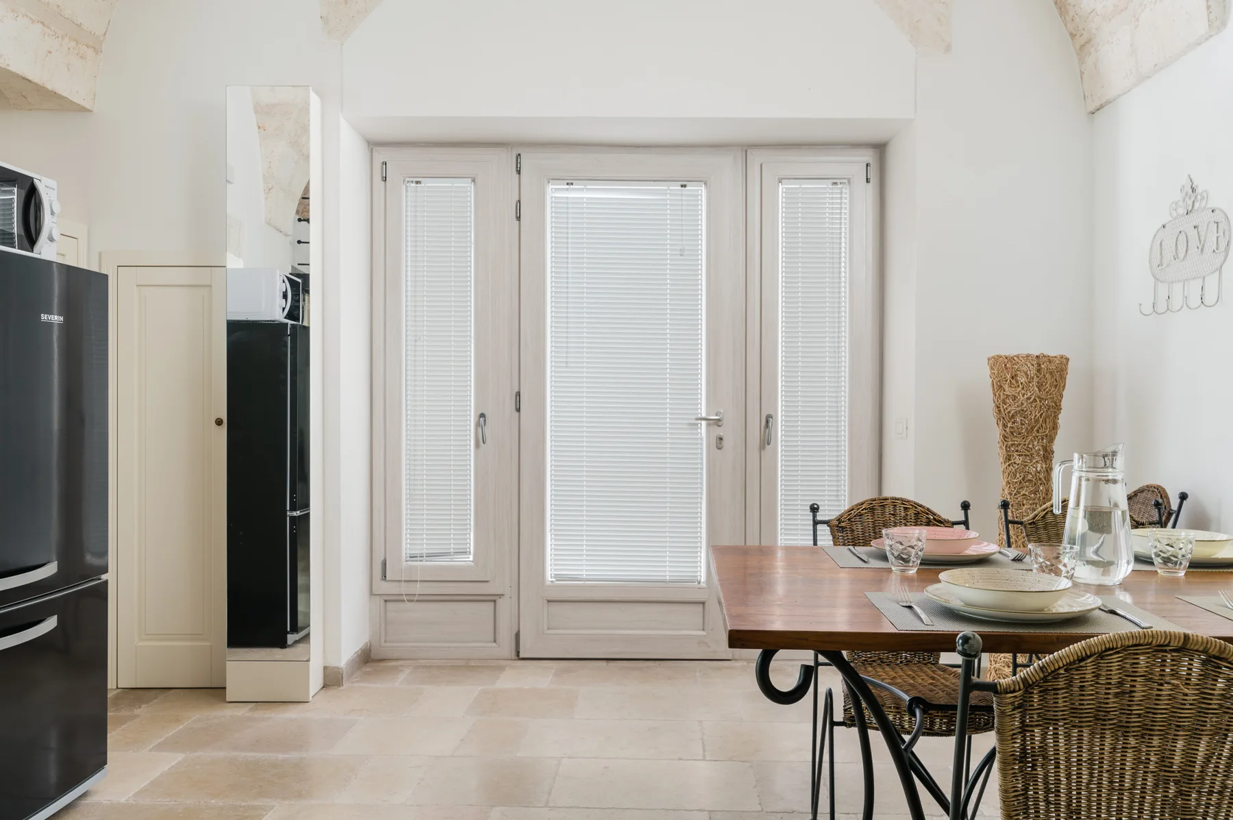 A dining area with a table and seating beside tall doors with blinds.