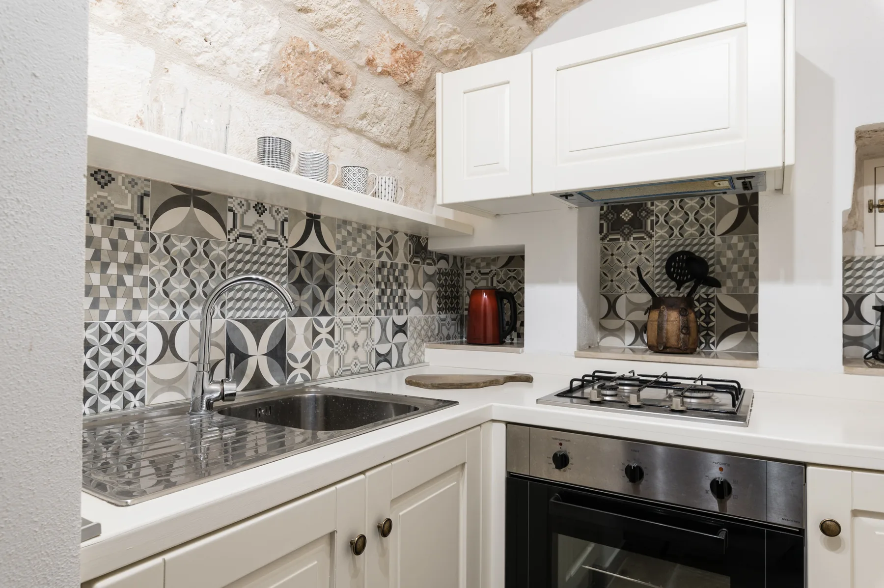 Una cocina compacta con gabinetes blancos, azulejos estampados y un horno integrado.