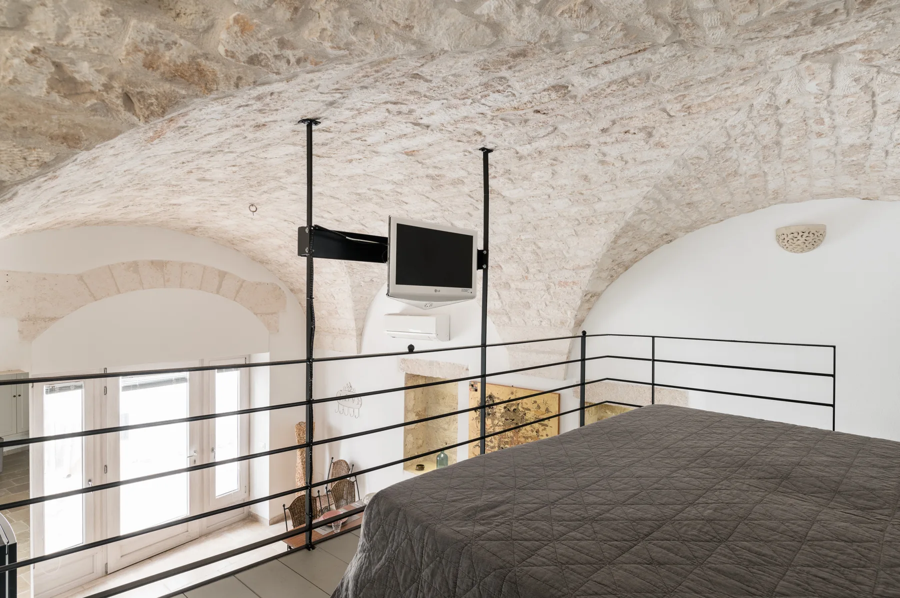Un dormitorio con una cama oscura junto a una barandilla negra bajo un techo de piedra.