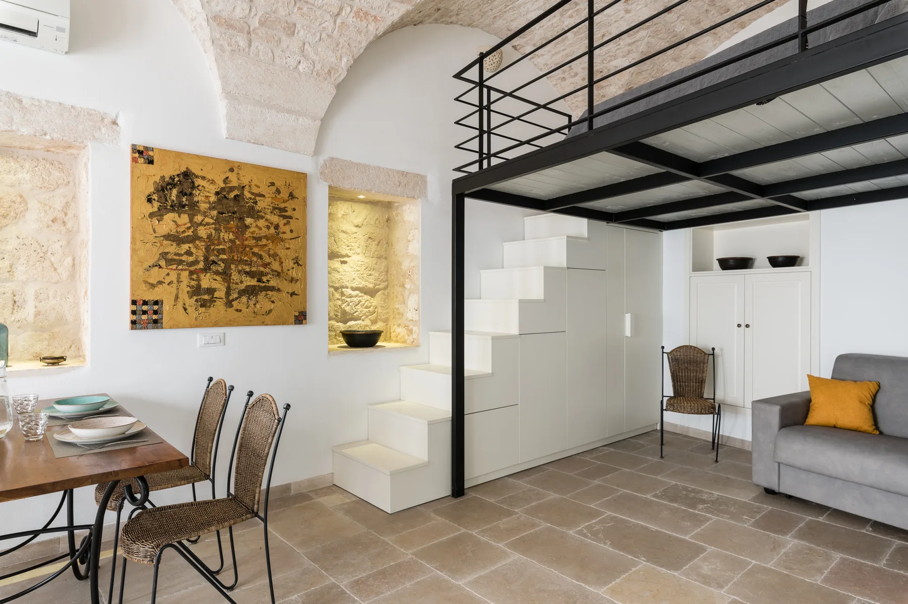 Una luminosa sala de estar y comedor tiene una cama en un altillo sobre una escalera integrada.